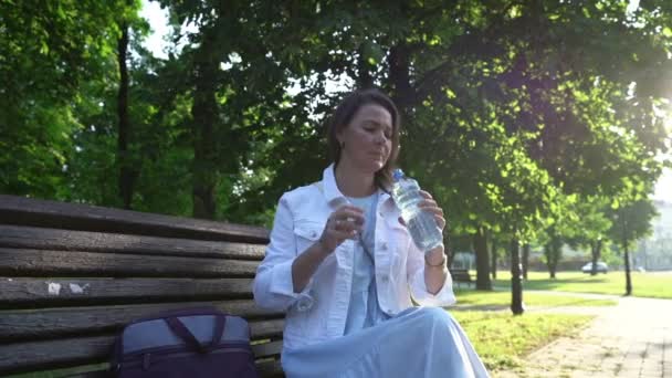 Mujer adulta en chaqueta blanca bebe agua de la botella en el parque — Vídeos de Stock