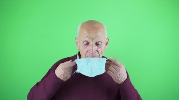 Old vulnerable man wearing medical face mask isolated on green background. — Stock Video