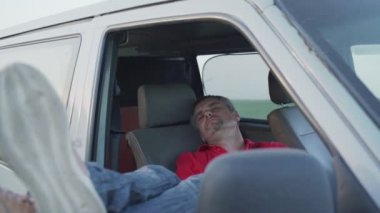 Minibüsün ön koltuğunda dinlenen gözleri kapalı yorgun bir adam.