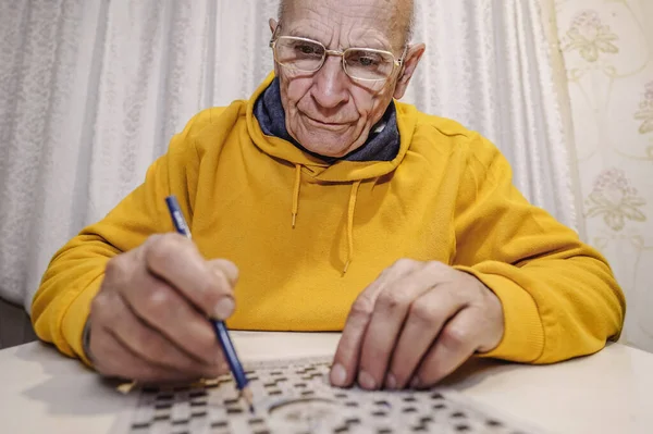 一个人戴眼镜，手里拿着铅笔解开纵横字谜 图库图片