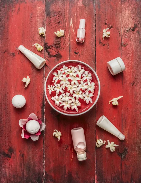 Red wellness set with bowl of water and flowers, jars with beaut — Stock Photo, Image