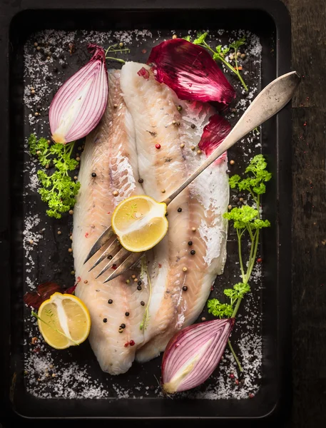 Raw fish with herb, spices and fork on black old backing tray, top view — Stock Photo, Image