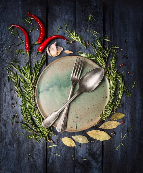 Cucchiaio e forchetta su piatto con cornice di erbe e spezie su tavolo di legno blu scuro, vista dall'alto — Foto Stock