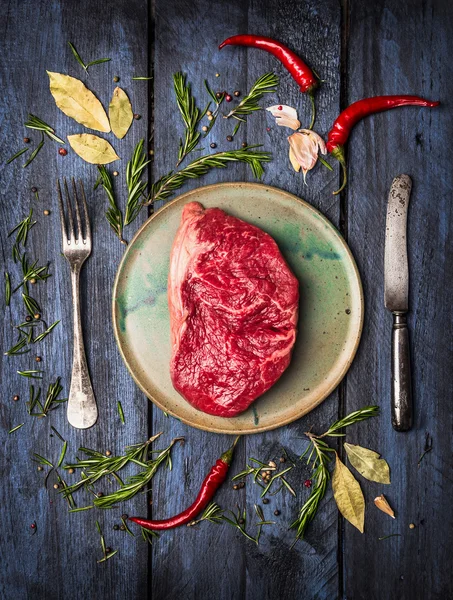 RAW ryggbiffen biff på tallrik med kniv och gaffel att lägga med örter och kryddor, blå trä bakgrund, ovanifrån — Stockfoto