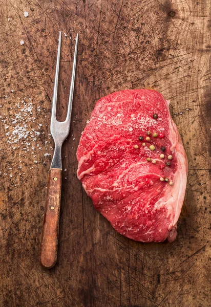 Carne cruda Filete Striploin con tenedor, sal y pimienta sobre fondo de madera viejo, vista superior —  Fotos de Stock