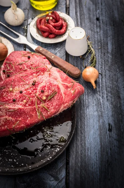 Viande de boeuf crue dans une poêle noire avec assaisonnements et sauce sur une table en bois bleu, préparation pour la friture — Photo