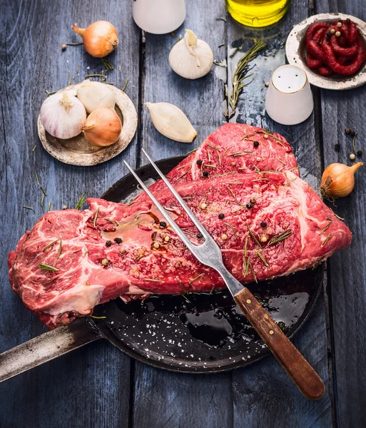 Stück rohes Rindfleisch mit Fleischgabel in alter Pfanne auf blauem Holztisch, Zubereitung zum Kochen — Stockfoto