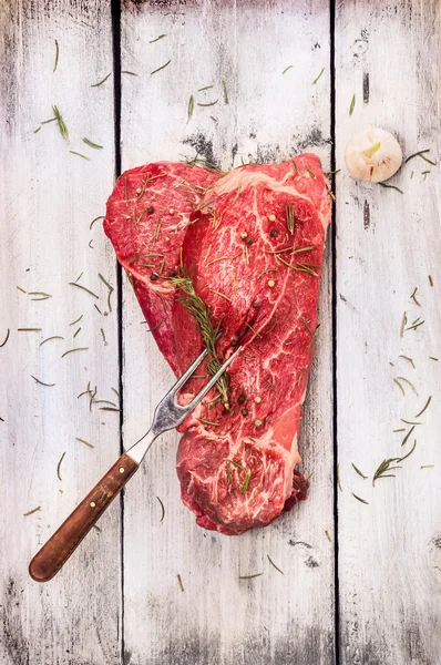 Rohes Rindfleisch mit Fleischgabel auf altem weißgrauem Holzhintergrund, Draufsicht — Stockfoto