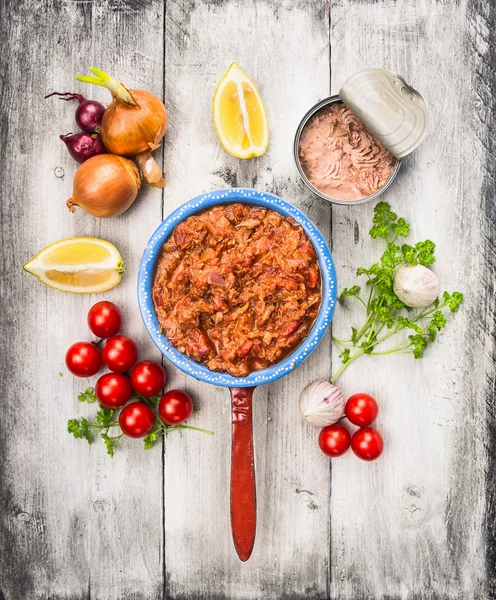 Ingredients for tomato sauce with tuna fish in old porridge pot on white wooden background, top view — Stock Photo, Image