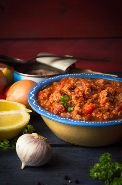 Tomato sause with tuna fish on rustic kitchen table with vegetables