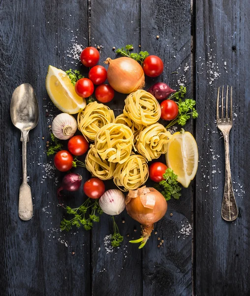 Macarrão tagliatelle com tomates, legumes e especiarias para molho de tomate, colher e garfo em fundo de madeira azul escuro, topo — Fotografia de Stock