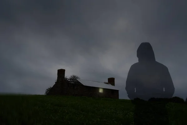 一个透明的 戴着鬼头的人影 在狂风暴雨的夜晚 看着一幢被毁得可怕的房子 窗户上有一盏灯 — 图库照片