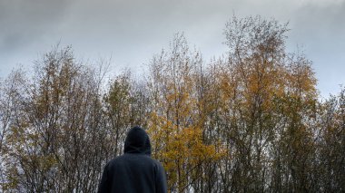 Gizemli kapüşonlu bir figür. Kasvetli bir kış gününde ağaçlara bakıyorum.