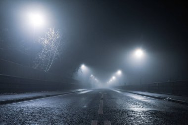 Düşük açı, atmosferik sisli kış gecelerinde bir yola ve sokak ışıklarına bakmak. İngiltere.