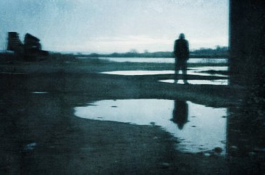 Huysuz bir figür, su birikintisine yansıyor. Endüstriyel bir bölgede bir köprünün altında duruyor. Bir grunge, soyut, düzenle.