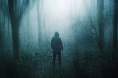 Huysuz, sisli bir kış gününde ürkütücü bir ormanın içinden geçen kapüşonlu bir figürün korku konsepti. Bir grunge, soyut düzenleme ile.