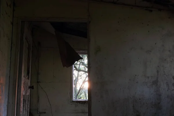 Looking out of a window at sunset in a spooky abandoned house. With decaying walls and broken ceiling.