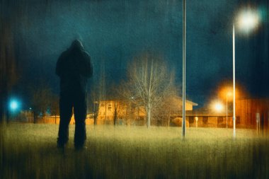 Kapüşonlu kapüşonlu bir figür, kameraya geri dönüyor. Sokak lambalarıyla çevrili bir kasabanın kıyısında dikiliyoruz. Bir grunge, bulanık düzenleme ile.