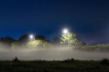 Mist floating above a field next to street lights on an atmospheric night