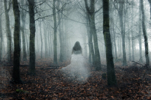 A supernatural concept of a ghostly woman wearing a long white dress, walking through a spooky, foggy forest in winter. With a grunge, vintage edit.