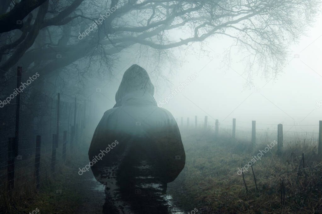 A double exposure of an atmospheric half transparent man looking at a foggy path in the countryside. On a moody foggy winters day. 