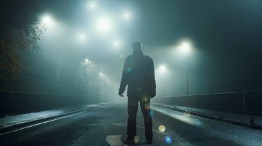 Geceleri sisli kış yollarının üzerinde süzülen ışıldayan kürelerin UFO konsepti. Siluetli bir figür, kameraya dönüp ışıklara bakıyor..                                