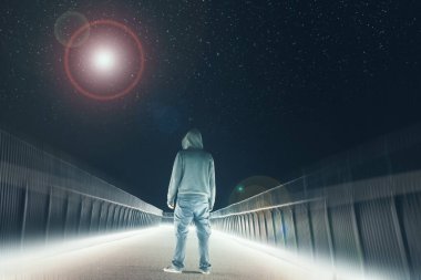 Yolda duran gizemli kapüşonlu bir figür. Geceleri parlak ışıklara karşı siluet. Gökyüzündeki parlak bir UFO 'ya bakıyorum.