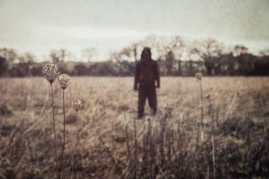 Kapüşonlu bir figürün korku konsepti. Kırsal kesimde duruyor. Bir grunge, vintage düzenleme ile