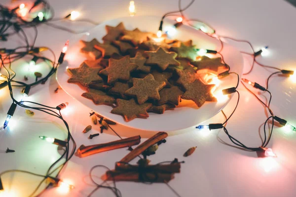 Moskou - 5 januari 2016: Gember kerstkoekjes in de vorm van een sterren op de tabel met kaneelstokjes en feestelijke verlichting in the Christmas Eve. — Stockfoto