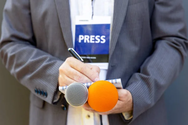 Correspondent or reporter at media event, holding microphone, writing notes. Journalism concept.