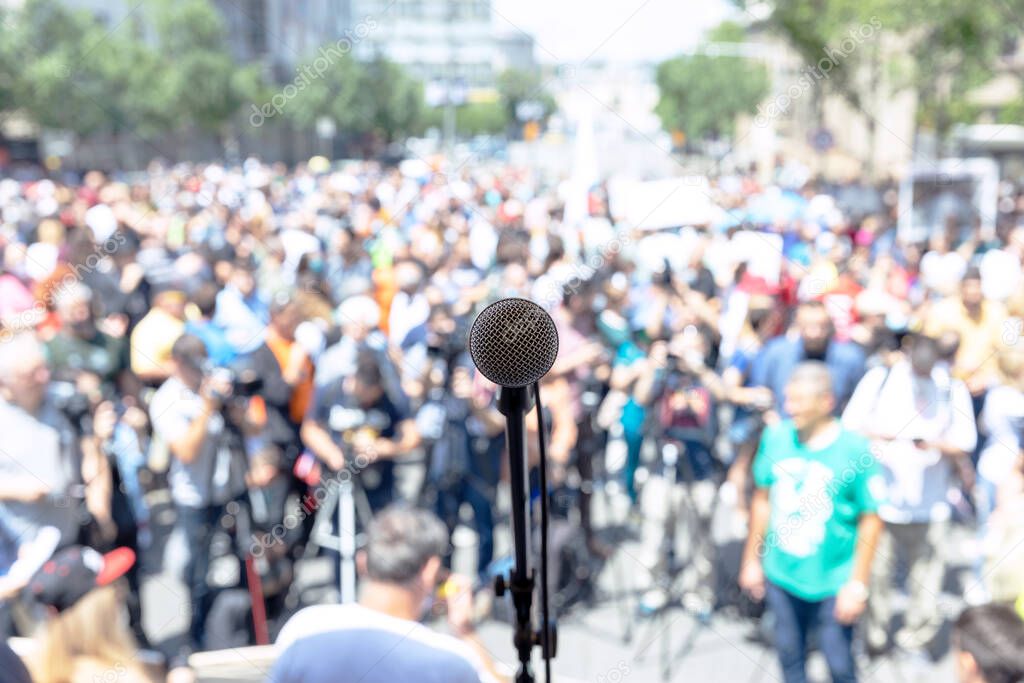 Focus on microphone, blurred group of people at mass protest or public demonstration in the background