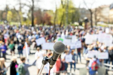 Mikrofona odaklan, arka planda kitlesel protestoda bulanık bir grup insan