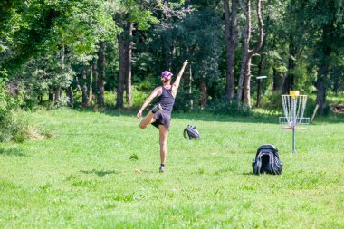 Doğada uçan disk golf oynayan genç bir kadın.