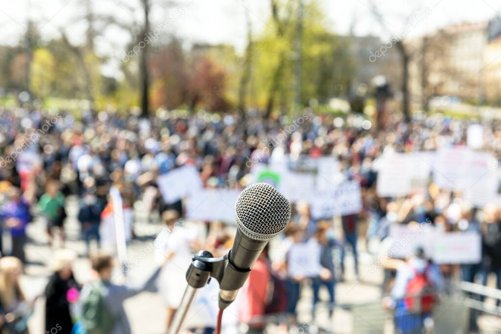 Focus on microphone, blurred group of people at mass protest in the background