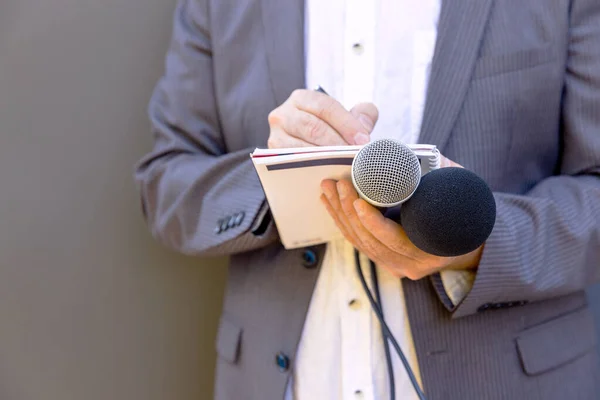 Journalist at media event or news conference, holding microphone, writing notes. Broadcast journalism concept.