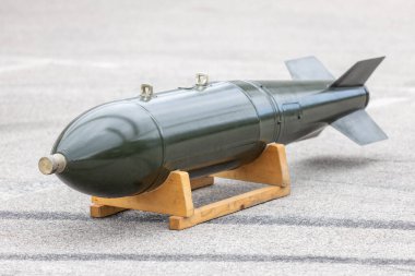 Military aerial unguided bomb on wooden support stand displayed outdoors on asphalt surface, vintage dumb bomb weaponry equipment for defense, war, aviation, training, museum, and historical technology