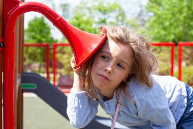 Oyun bahçesindeki ses kanallarını dinleyen meraklı genç kız, açık hava oyun ekipmanlarını, çocukluk merakını, hayal gücünü, öğrenmeyi ve parlak bir park ortamında duyusal oyunu keşfediyor.