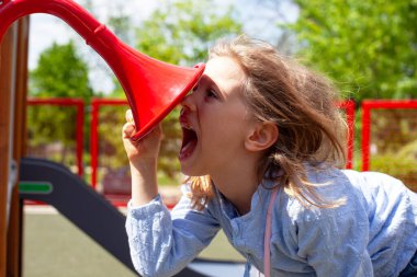 Parlak bir park ortamında yaratıcılık, iletişim ve çocukluk merakını ifade eden yaratıcı açık hava oyunlarıyla çocuk parkının ses tüpüne bağıran, sesi ve sesi keşfeden genç kız.