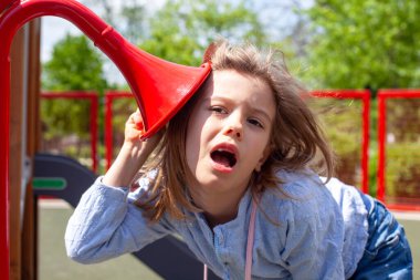 Çocuk, oyun alanındaki ses tünelinde, işitme, ses tonları ve hayal gücüne odaklanmış, dışarıda oyun oynarken duyusal algıları, yaratıcılığı ve işitsel keşifleri keşfediyor.