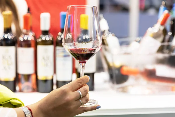 Şarap tatma etkinliği sırasında tutulan kırmızı şarap kadehleri, zarif cam eşyalar, şaraphane atmosferi, gurme deneyimi, misafirperverlik ve arka planda bulanık şişeler bulunan özel içecek kültürü.