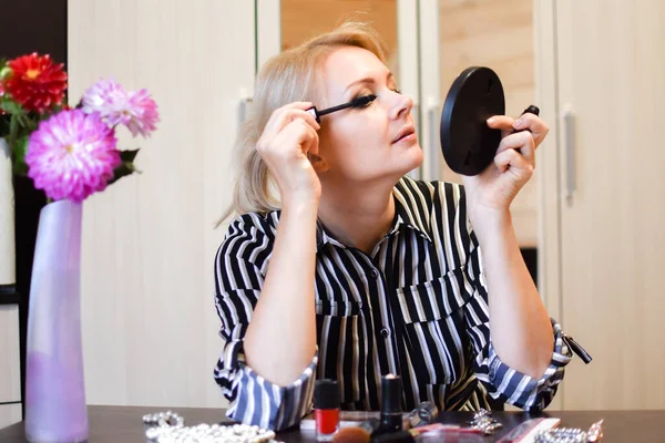 woman at cosmetic table paints her eyes. business woman doing makeup at home.