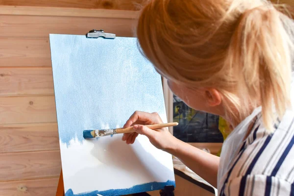 Woman artist paints picture on canvas in wooden house. Hobby painting