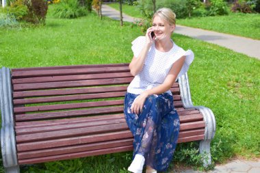 Genç bir kadın parkta bankta oturuyor ve internetten konuşuyor..