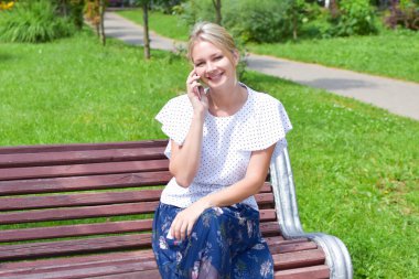 Genç bir kadın parkta bankta oturuyor ve internetten konuşuyor..