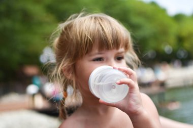 Küçük kız açık hava memesinden su içiyor. Elinde bir şişe su olan küçük bir kız.