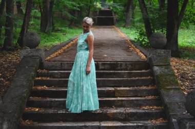 Yeşil orman parkında uzun açık yeşil elbiseli zarif bir kız..