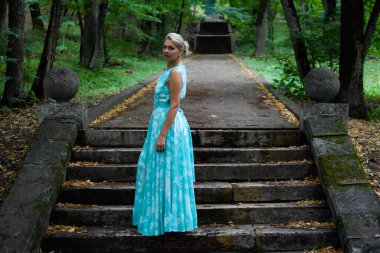 Yeşil orman parkında uzun açık yeşil elbiseli zarif bir kız..