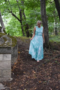 Yeşil orman parkında uzun açık yeşil elbiseli zarif bir kız..