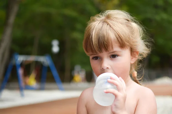 Holčička pije drink z bradavky venku. batole dívka s lahví vody — Stock fotografie