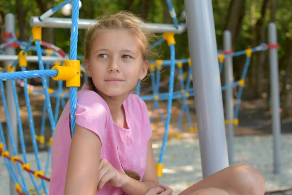 Грустная девочка летом сидит одна на детской площадке. Одинокая девочка-подросток скучает — стоковое фото